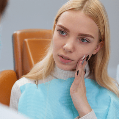 Woman at the orthodontist, holding her jaw in pain, representing how to handle orthodontic emergencies