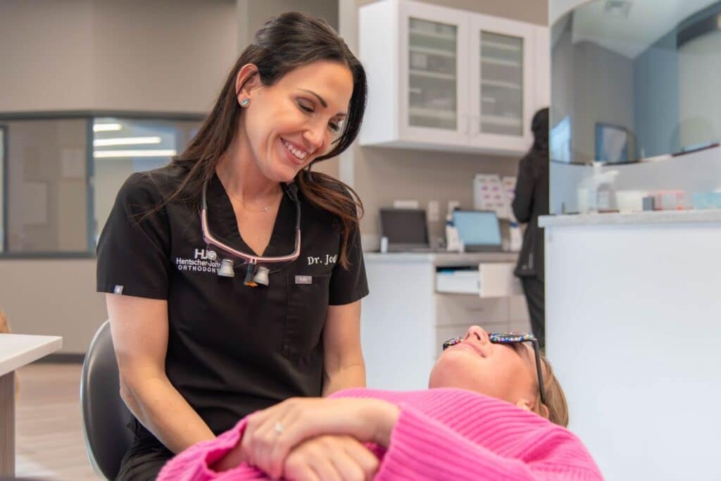 Dr. Jodi smiling at a patient in a pink sweater during orthodontic treatment at a top-rated practice.