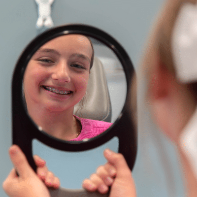 Teenage girl smiling with braces in a mirror at hjo, representing how phase one orthodontics works